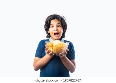 Cheerful Indian Asian Kid Boy Eating Potato Chips Or Wafers In A Bowl,  Standing Isolated Against White Background