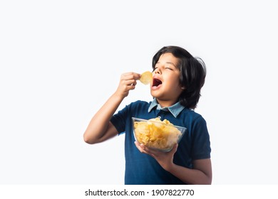 Cheerful Indian Asian Kid Boy Eating Potato Chips Or Wafers In A Bowl,  Standing Isolated Against White Background