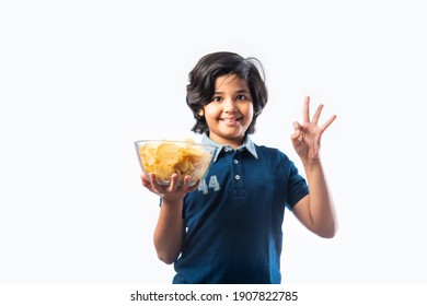 Cheerful Indian Asian Kid Boy Eating Potato Chips Or Wafers In A Bowl,  Standing Isolated Against White Background