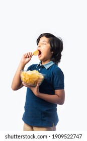 Cheerful Indian Asian Kid Boy Eating Potato Chips Or Wafers In A Bowl,  Standing Isolated Against White Background