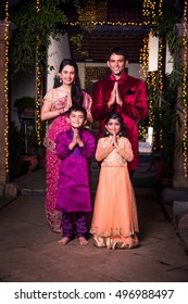 Cheerful Indian Family Welcoming On Diwali Night Outside Home With Diwali Lighting, Indian Couple And Kids Or People In Namaskar Pose Welcoming Guests On Diwali Celebration Or Festival Night