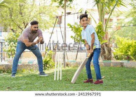 Cheerful indian father encouraging son from behind while playing cricket game at park - concept of Motivation, Guidance and parental support
