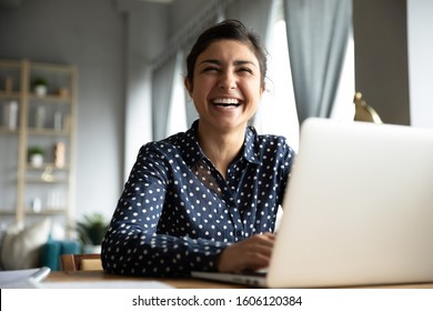 Cheerful indian girl student professional laughing looking away sit with laptop computer at home office table, positive hindu woman having fun enjoy sincere emotion laughter studying working on pc