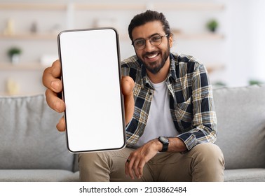 Cheerful Indian Guy Showing Smartphone With Big Blank White Screen At Camera, Happy Young Eastern Man Recommending New Mobile App Or Website While Sitting On Couch At Home, Creative Collage, Mockup - Shutterstock ID 2103862484