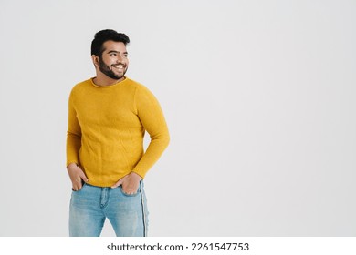 Cheerful indian guy wearing yellow sweater looking away at copy space while standing with hands in pockets isolated over white studio wall - Powered by Shutterstock