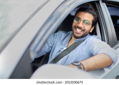 Cheerful Indian Man Driving Car, Shot From Outside, Going On Trip During Summer Vacation, Side View, Copy Space. Happy Indian Guy In Casual Outfit And Glasses Driving His Brand New Nice Car, Closeup