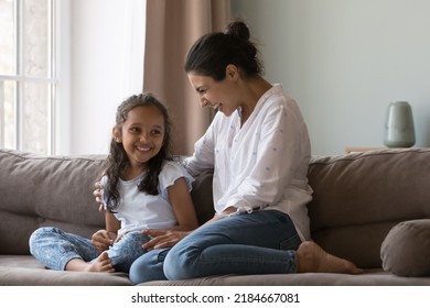 Cheerful Indian Mom Cuddling Happy Little Daughter On Couch At Home With Love, Care, Gratitude, Talking To Kid, Smiling, Laughing, Having Fun, Enjoying Motherhood, Family Leisure Time