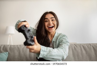 Cheerful Indian Woman Enjoying Videogame On Playstation, Having Fun Indoors. Excited Millennial Gamer With Joystick Playing Computer Arcade. Stay Home Hobbies And Activities