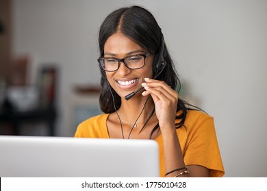 Cheerful indian woman in smart working from home. Happy middle eastern girl working as customer service representative with laptop. Smiling young woman with headset doing video call at home. 