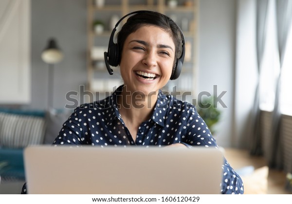 Cheerful indian woman wear headset laugh using\
laptop video stream conference call teach online, happy ethnic girl\
student gamer tutor have fun watch webinar web cam education\
entertainment concept
