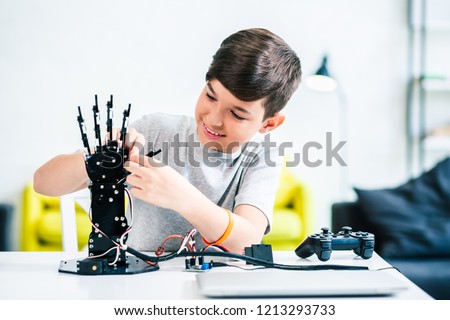 Cheerful ingenious boy testing his robotic creation while preparing for engineerign classes
