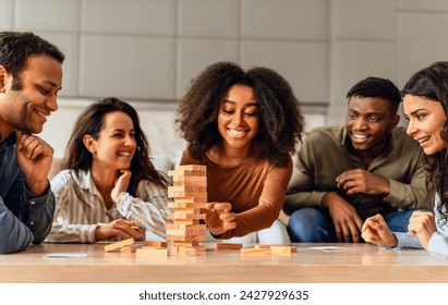 Cheerful international students group around table in kitchen engaging in joyful board game, building wooden tower together for fun, spending spare time on weekend, having home party - Powered by Shutterstock