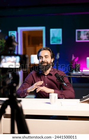 Cheerful internet star talking in front on professional camera and quality mic in studio, discussing with viewers. Joyful man using high tech recording gear to record social media video