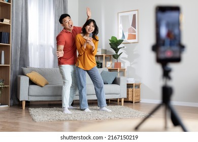 Cheerful japanese couple broadcasting while having fun together at home, expressive asian man and woman vloggers singing karaoke and dancing in front of smartphone camera, full length shot - Powered by Shutterstock