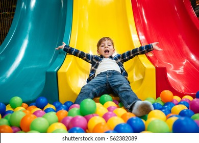 Cheerful joyful little boy playing on slide and pool with colorful balls - Shutterstock ID 562382089