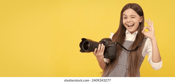 cheerful kid girl take photo with digicam show ok gesture, photography. Child photographer with camera, horizontal poster, banner with copy space.