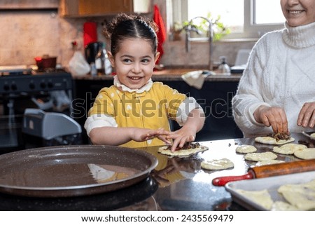 Cheerful kid helping mother in preparing pastries in kitchen , preparing food together