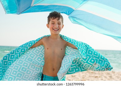 A Cheerful Kid On The Beach On A Sunny Summer Day Wrapped In A Bright Beach Towel.