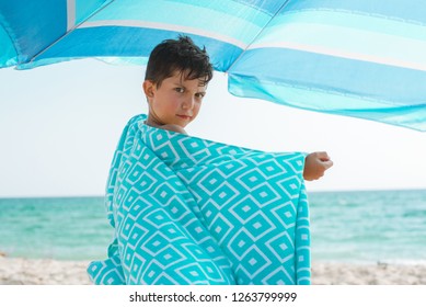 A Cheerful Kid On The Beach On A Sunny Summer Day Wrapped In A Bright Beach Towel.