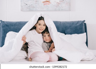 Cheerful Kid Sitting Under Blanket With Cute Toddler Brother 