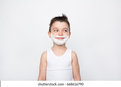 Cheerful Kid In Tank Top And Shaving Foam On Face Smiling Away On White Background,