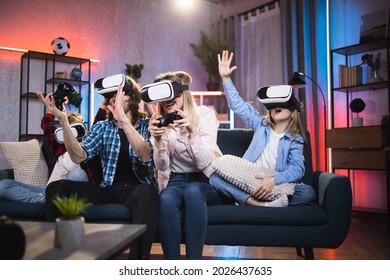 Cheerful kids with their young parents wearing 3D goggles while playing video games at home. Modern family sitting on couch and spending time in virtual reality. - Powered by Shutterstock