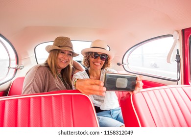 Cheerful Ladies Caucasian And Selfie With Modern Smart Phone Inside An Old Red Vintage Car. Modern And Old Things Related. Internet And Social Networks Share Concept