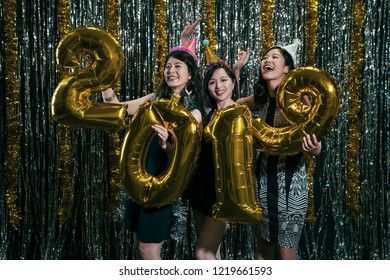 cheerful ladies showing gold number 2019 balloon at nightclub. new year eve party countdown with funny girls on the stage dancing with hats. young people dico night lifestyle concept.