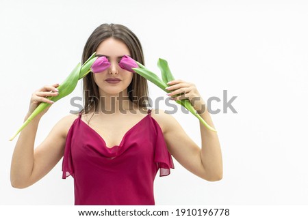 Cheerful lady fooling around hiding her eyes behind a tulip flowers over white baackground.