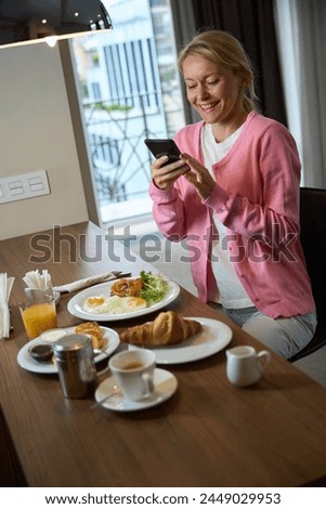 Cheerful lady reading something on cellphone in suite during mealtime
