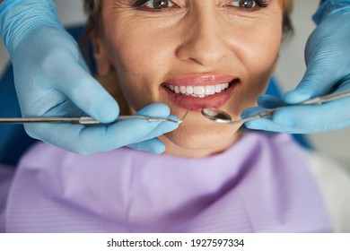 Fröhliche Dame, die sich ihre weißen Zähne in einem Lächeln zeigt, mit zwei Händen, die Zahninstrumente in den Mund bringen