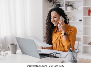 Cheerful Lady Talking On Cellphone Holding Paper Sitting At Desk And Using Laptop Computer Working Online In Modern Office. Entrepreneurship And Business Career, Distance Freelance Job Concept - Powered by Shutterstock