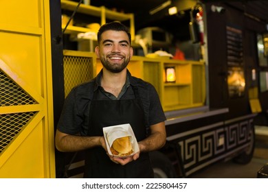 Cheerful latin chef at the food truck ready to serve fast food and showing a delicious sandwich - Powered by Shutterstock