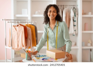 Cheerful latin fashion designer standing in well-lit studio, holding packaged product and color swatches, embodying creativity and entrepreneurial spirit in modern fashion atelier - Powered by Shutterstock