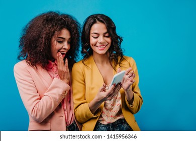 Cheerful Latin Girl With Wavy Hairstyle Making Selfie. Glamorous Friends Chilling In Studio.