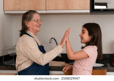 Cheerful latin grandmother and granddaughter with big smile giving a high five in kitchen home, indoors. Family, happiness, multi generation concept. - Powered by Shutterstock