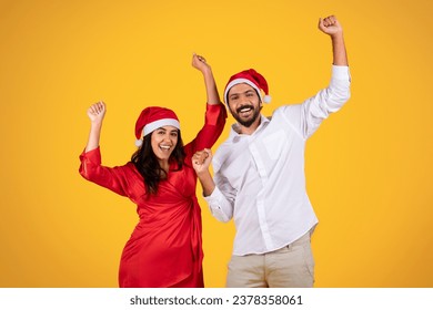 Cheerful latin man and woman in Santa hats, celebrating holiday with raised hands, festive cheer and excitement, dance, isolated on orange studio background. Xmas, New Year mood - Powered by Shutterstock