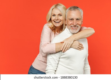 Cheerful laughing funny couple two friends elderly gray-haired man blonde woman in white pink casual clothes standing hugging looking camera isolated on bright orange color background studio portrait
