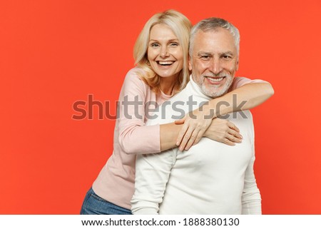 Cheerful laughing funny couple two friends elderly gray-haired man blonde woman in white pink casual clothes standing hugging looking camera isolated on bright orange color background studio portrait