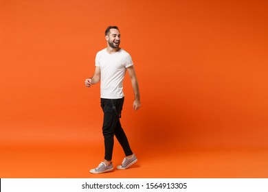 Cheerful Laughing Young Man In Casual White T-shirt Posing Isolated On Bright Orange Wall Background Studio Portrait. People Sincere Emotions Lifestyle Concept. Mock Up Copy Space. Looking Aside