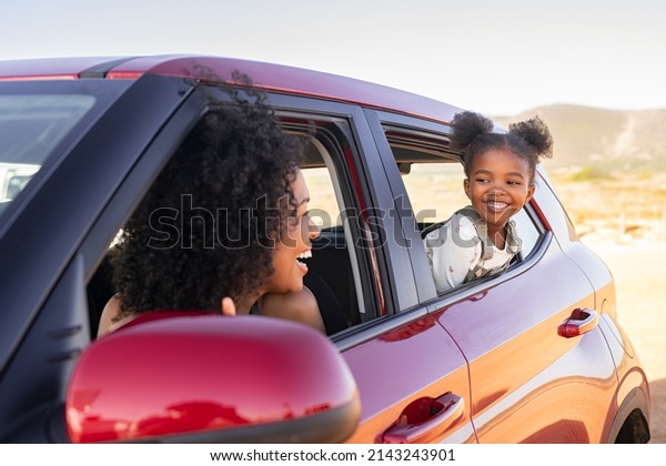 Cheerful little african american daughter sitting on\
back seat of car looking at mother from mirror while travelling.\
Young fun woman with cheerful female kid enjoying road trip. \
Traveling in car.