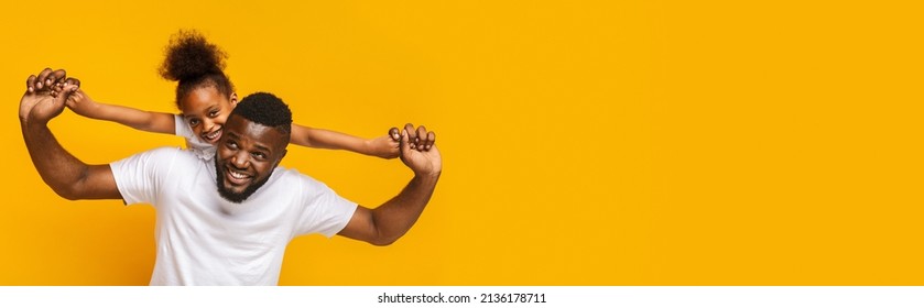Cheerful little african american girl with bushy hair riding on daddy's back young man, orange studio background, panorama with copy space, web-banner for family, fatherhood concept - Shutterstock ID 2136178711