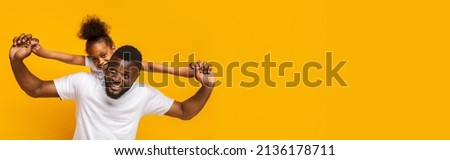 Cheerful little african american girl with bushy hair riding on daddy's back young man, orange studio background, panorama with copy space, web-banner for family, fatherhood concept