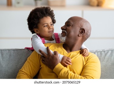 Cheerful little black girl play with older grandfather from back, hugging man at home interior. Family, people, relationships of generations during covid-19 lockdown. Positive active at living room