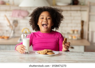 Cheerful Little Black Girl Sitting At Table Enjoying Milk And Cookies, Cute African American Child Having Snacks In Kitchen, Having A Bite With Healthy Calcium Drink And Homemade Pastry, Closeup