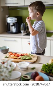 Cheerful Little Boy Cooking Fresh Healthy Breakfast At Kitchen With Avocado, Cottage Cheese, Fruit And Berries. Funny Male Kid Trying Eating Blueberry Ingredient At Cuisine Preparing Sandwich