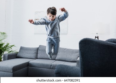 Cheerful little boy in pajamas jumping on couch at home - Powered by Shutterstock