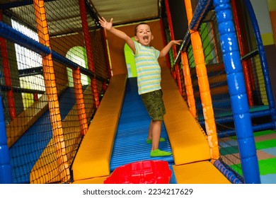 Cheerful little boy playing in the children's entertainment center.Cute child boy near a roller coaster with a plastic red sledge on the playground in the children's play center	