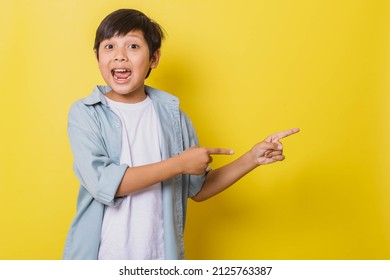 Cheerful little boy screaming while pointing sideways isolated on yellow background with copy space