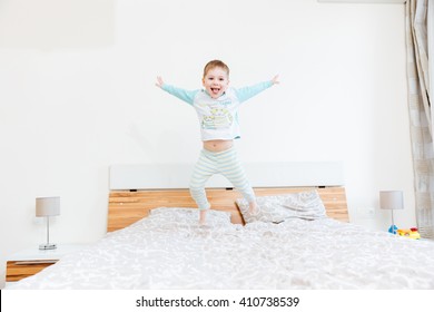 Cheerful little boy showing tongue and jumping on bed at home 